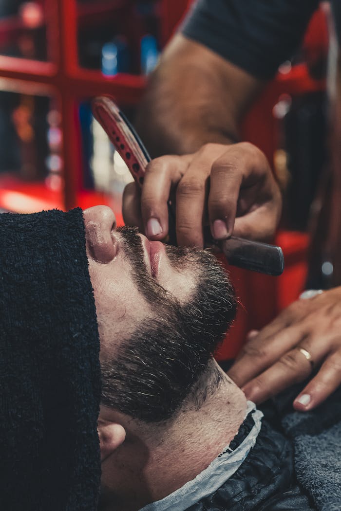 A barber skillfully shaves a mans beard using a straight razor at a barbershop.