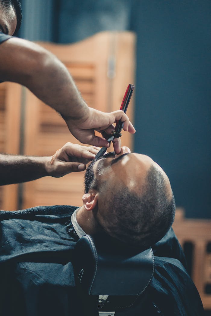 Close-up of a barber expertly shaving a mans beard indoors, showcasing precision and care.