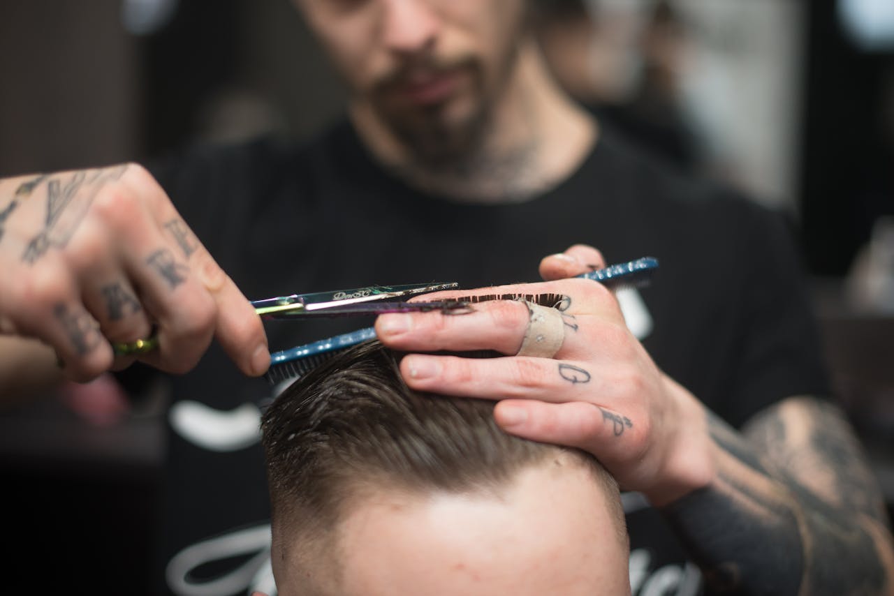 services-02 A tattooed barber provides a precise haircut in a modern barbershop setting.